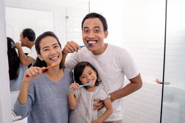 An Asian family smiles and brushes their teeth together